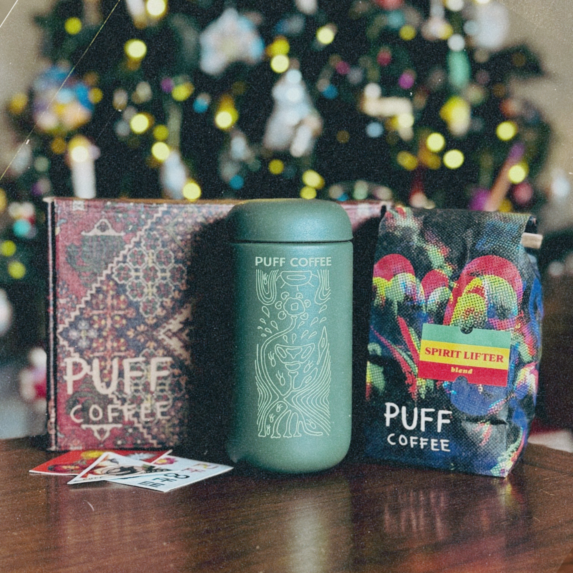 Green coffee tumbler with 'Puff Coffee' packaging in front of a decorated Christmas tree.