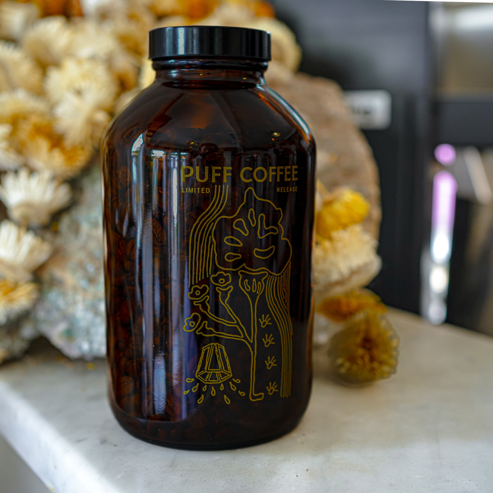 Brown glass jar with 'Puff Coffee' branding on a surface with decorative elements in the background